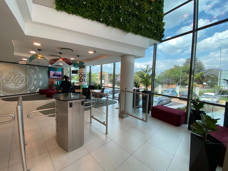 Modern commercial building entrance lobby featuring floor-to-ceiling windows, secure turnstile access control, and a prominent vertical garden wall.