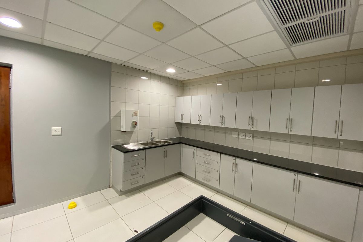 A clean, functional commercial kitchen area featuring extensive built-in cabinetry, dark countertops, a stainless steel sink, and professional tiled finishes.