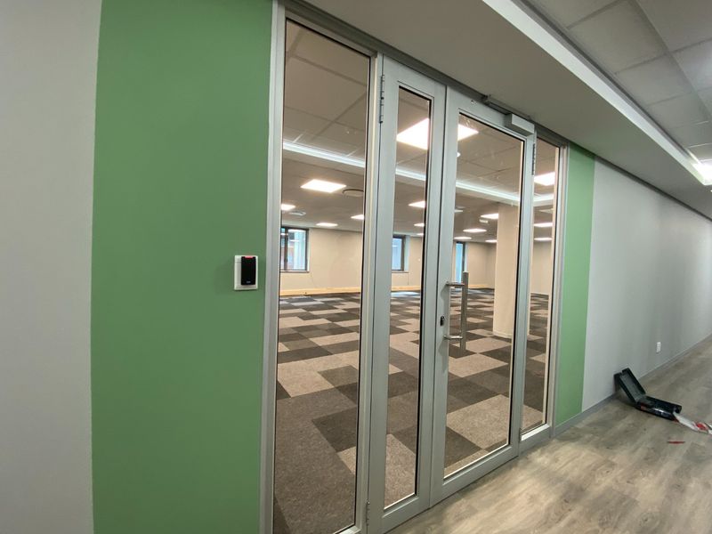 A modern, vacant commercial office space featuring glass double doors, access control, carpet tiles, and recessed LED lighting in a suspended ceiling.