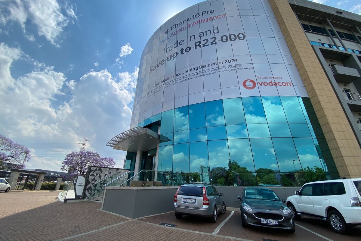 Modern commercial building facade featuring a large glass curtain wall, paved parking area, and a prominent entrance canopy.