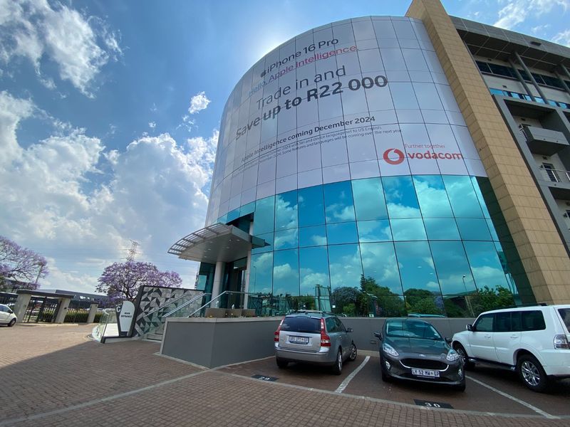 Modern commercial building facade featuring a large glass curtain wall, paved parking area, and a prominent entrance canopy.
