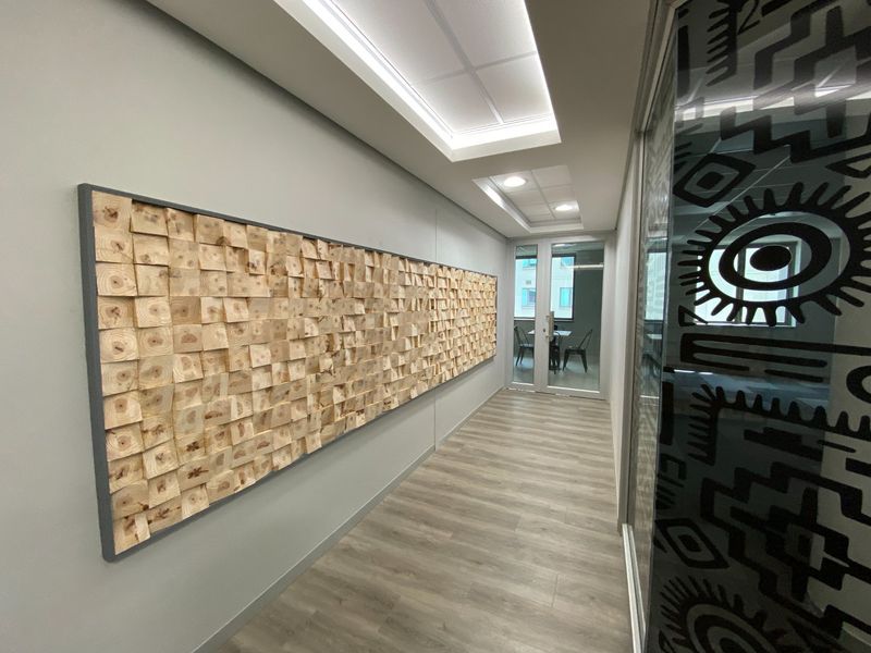Modern commercial hallway featuring wood-look laminate flooring, recessed ceiling lighting, and a decorative timber block wall feature with glass partition access.