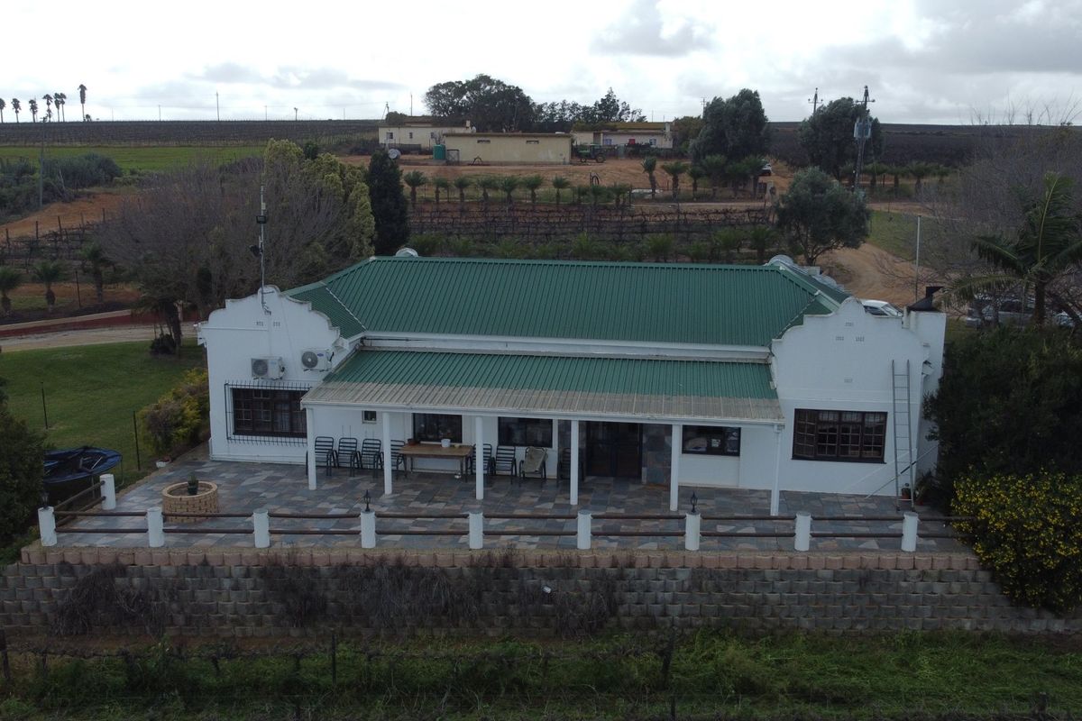 Aerial view of a farm homestead featuring a green corrugated metal roof, a spacious stone-paved patio, and a retaining wall overlooking the surrounding agricultural land.