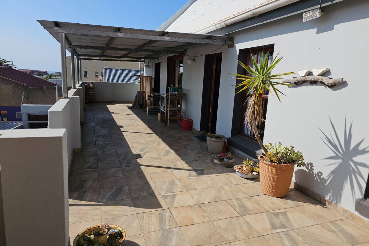 A spacious covered balcony featuring tiled flooring and a metal roof structure, offering an outdoor area accessible via sliding doors.