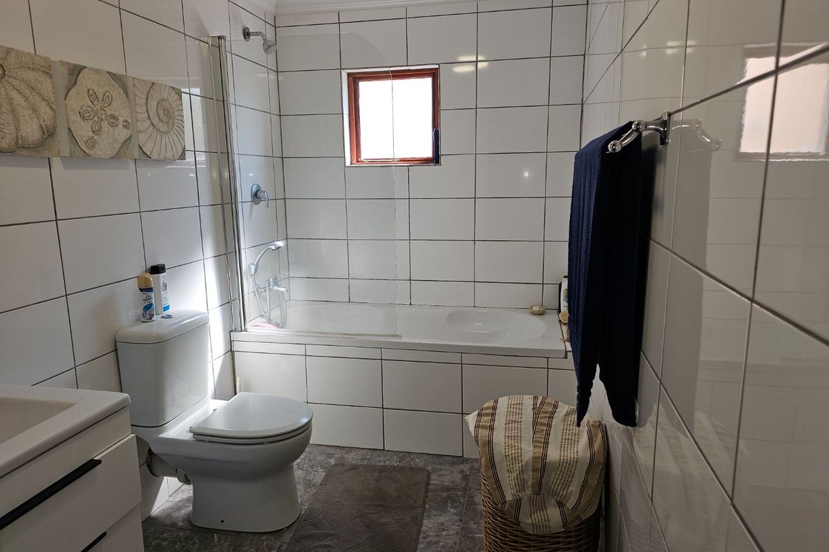 A functional bathroom featuring a built-in bathtub with a glass shower screen, a toilet, and a vanity basin with white wall tiling.
