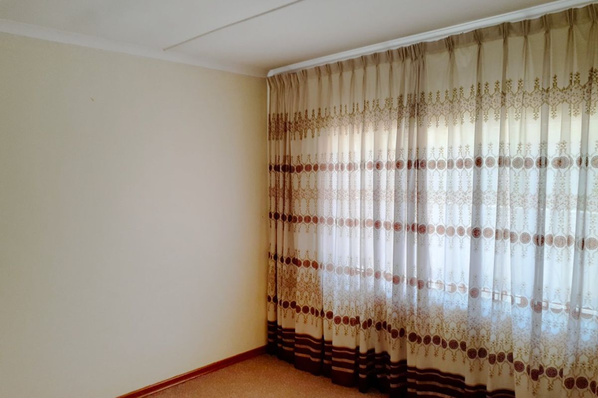 A clean, empty bedroom featuring neutral wall finishes, carpeted flooring, and installed curtain tracks, providing a blank canvas for personalization.