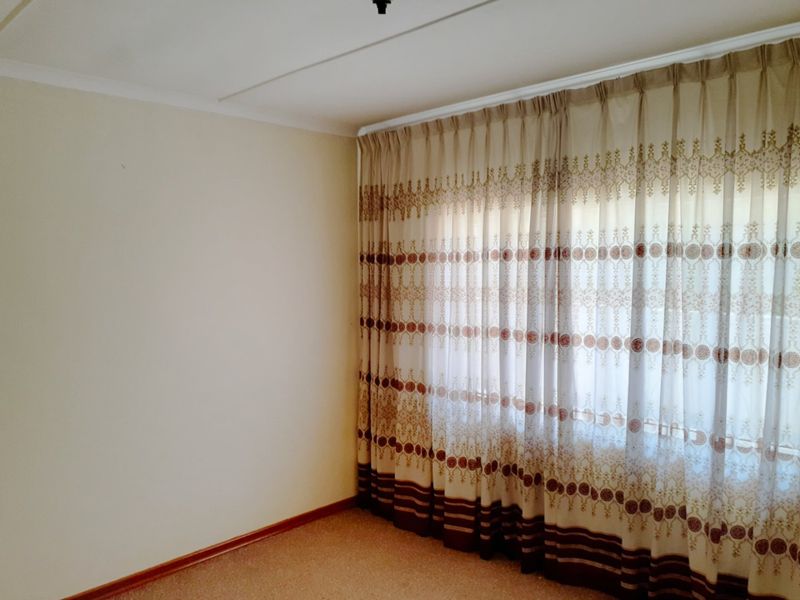 A clean, empty bedroom featuring neutral wall finishes, carpeted flooring, and installed curtain tracks, providing a blank canvas for personalization.