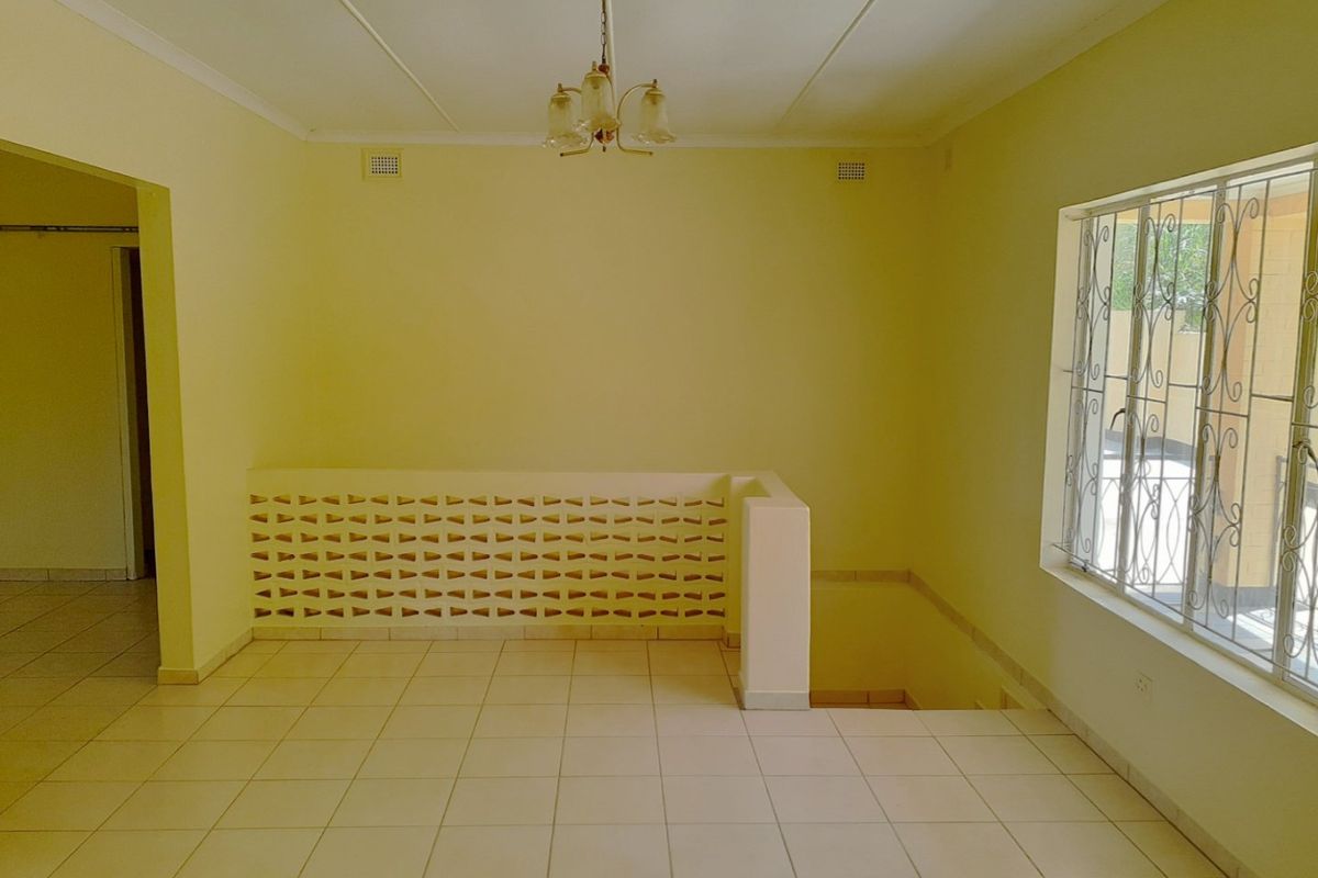 An empty, open-plan living area featuring tiled flooring, a decorative breeze block partition, and a staircase void with security-barred windows.