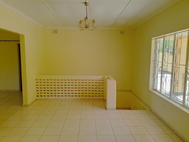 An empty, open-plan living area featuring tiled flooring, a decorative breeze block partition, and a staircase void with security-barred windows.