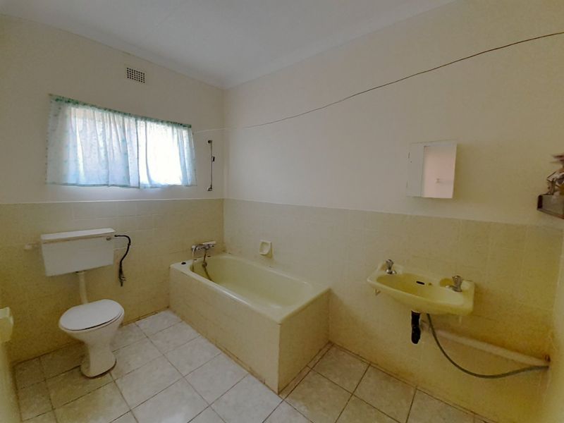 A dated bathroom featuring a bathtub, wall-mounted basin, and toilet with original tiling, offering significant potential for a modern renovation.
