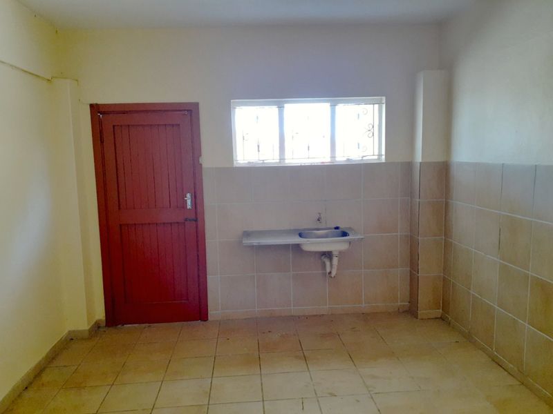 A functional, empty scullery area featuring a stainless steel sink, tiled splashback, and tiled flooring, ready for renovation or utility use.
