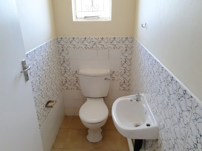 A compact guest bathroom featuring a standard toilet, wall-mounted basin, and decorative tiled splashback.