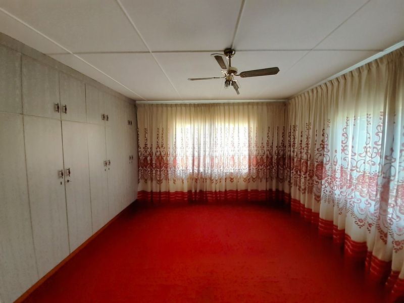 Spacious bedroom featuring extensive built-in cupboards, a ceiling fan, and wall-to-wall carpeting, offering a blank canvas for renovation.