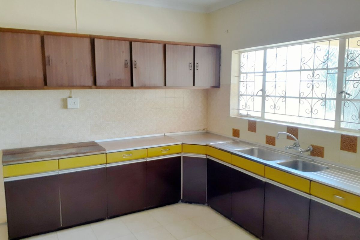 A functional kitchen featuring dated cabinetry, laminate countertops, a double stainless steel sink, and tiled splashbacks, offering potential for a modern renovation.