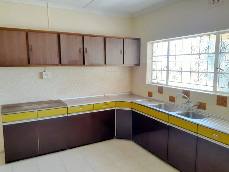 A functional kitchen featuring dated cabinetry, laminate countertops, a double stainless steel sink, and tiled splashbacks, offering potential for a modern renovation.