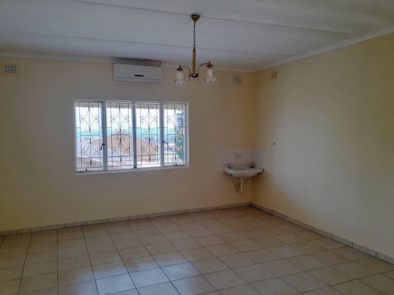 An empty living area featuring tiled flooring, a wall-mounted air conditioning unit, and a small basin, offering a blank canvas for renovation.