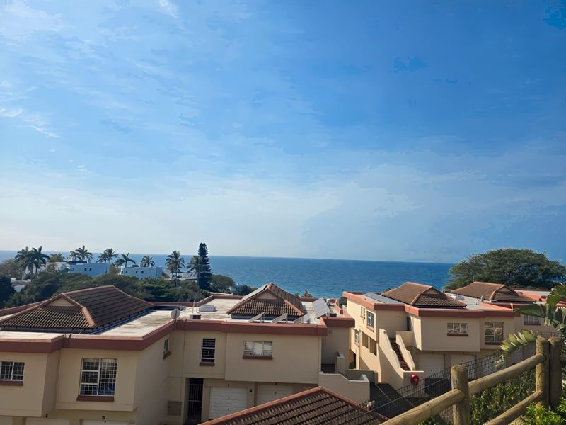 Elevated view overlooking a residential complex with tiled roofs and solar panels, featuring a scenic ocean horizon in the background.