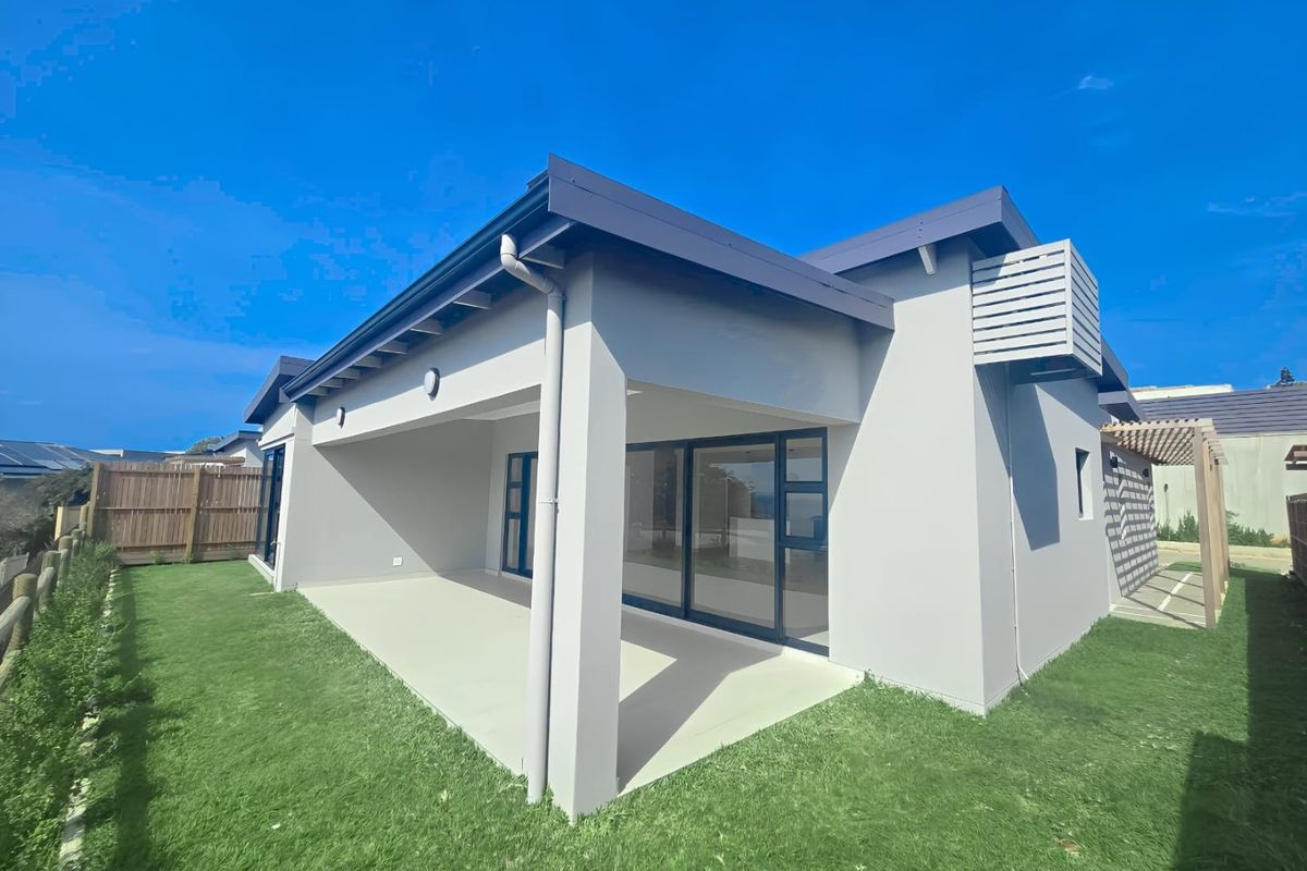Rear view of the property featuring a covered patio, sliding glass doors, and a well-maintained lawn with timber fencing.