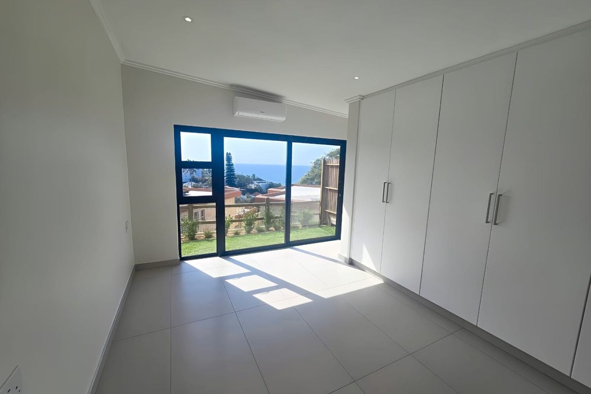 A bright, modern bedroom featuring neutral tiled flooring, extensive built-in storage, air conditioning, and large sliding doors opening to a scenic outdoor view.