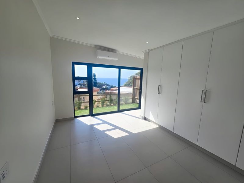 A bright, modern bedroom featuring neutral tiled flooring, extensive built-in storage, air conditioning, and large sliding doors opening to a scenic outdoor view.