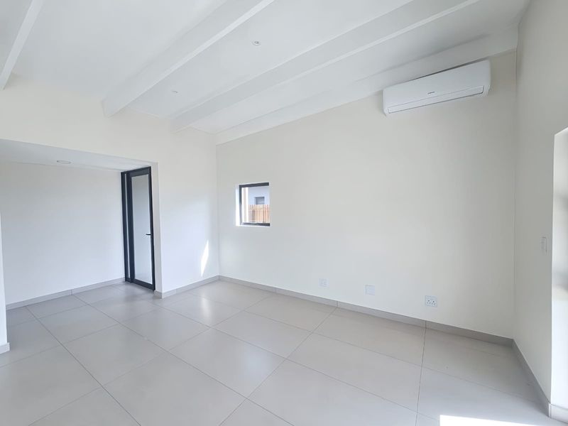 A bright, modern, and empty living area featuring tiled floors, exposed ceiling beams, and a wall-mounted air conditioning unit.