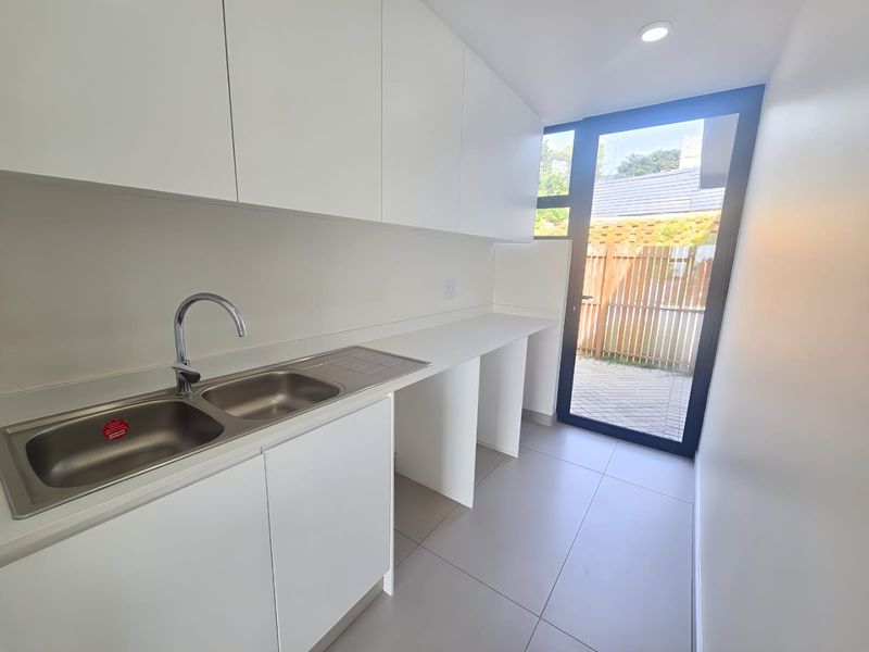 Modern, clean-lined scullery featuring white cabinetry, double stainless steel sink, tiled flooring, and direct access to the rear outdoor area.