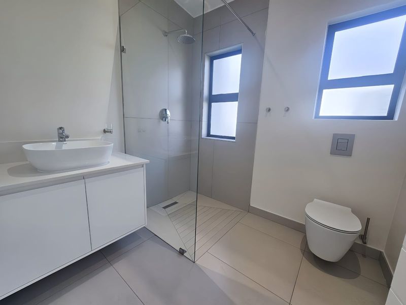Modern bathroom featuring a floating vanity with vessel sink, a spacious walk-in shower with glass screen, and a wall-mounted toilet with concealed cistern.