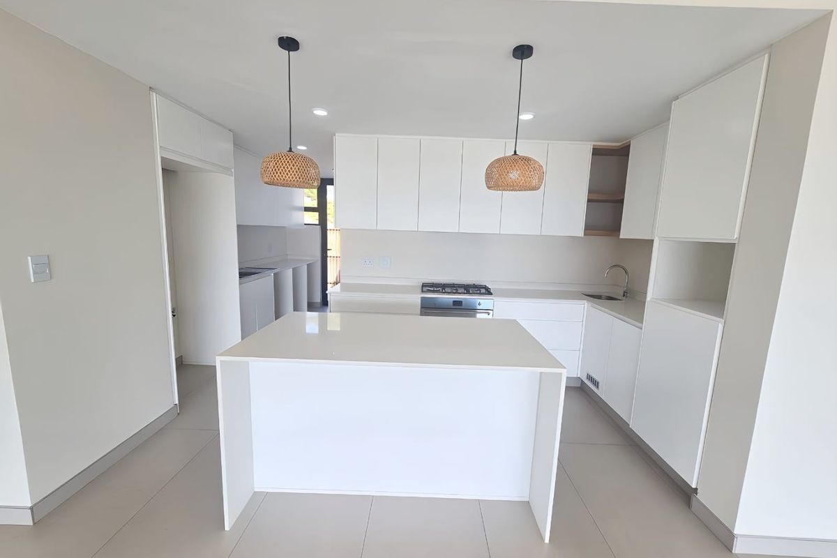 Modern, minimalist kitchen featuring a central island, white cabinetry, gas hob, and sleek tiled flooring in a bright, open-plan layout.