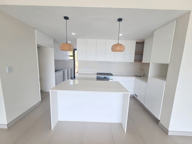 Modern, minimalist kitchen featuring a central island, white cabinetry, gas hob, and sleek tiled flooring in a bright, open-plan layout.