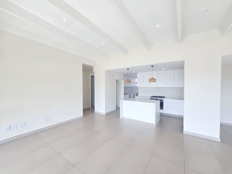 Spacious open-plan living area featuring a modern kitchen with a central island, built-in appliances, sleek cabinetry, and exposed ceiling beams throughout.