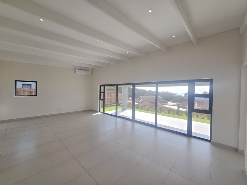 Spacious, light-filled living area featuring neutral tiled floors, exposed beam ceilings, and large sliding doors opening to an outdoor patio.