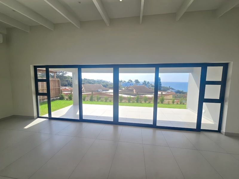 Spacious living area featuring large sliding glass doors that open onto a patio with scenic coastal views and modern tiled flooring.
