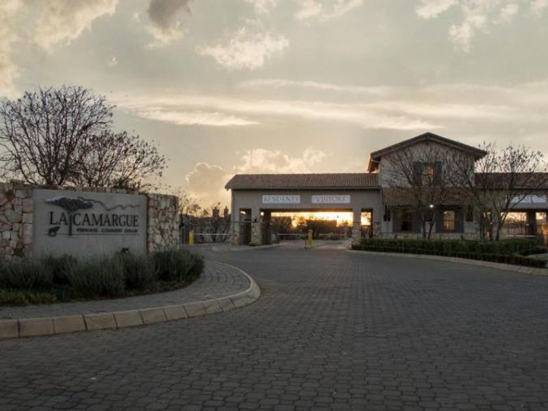 The secure entrance gatehouse of La Camargue Private Country Estate, featuring stone masonry, paved driveway, and controlled access points.
