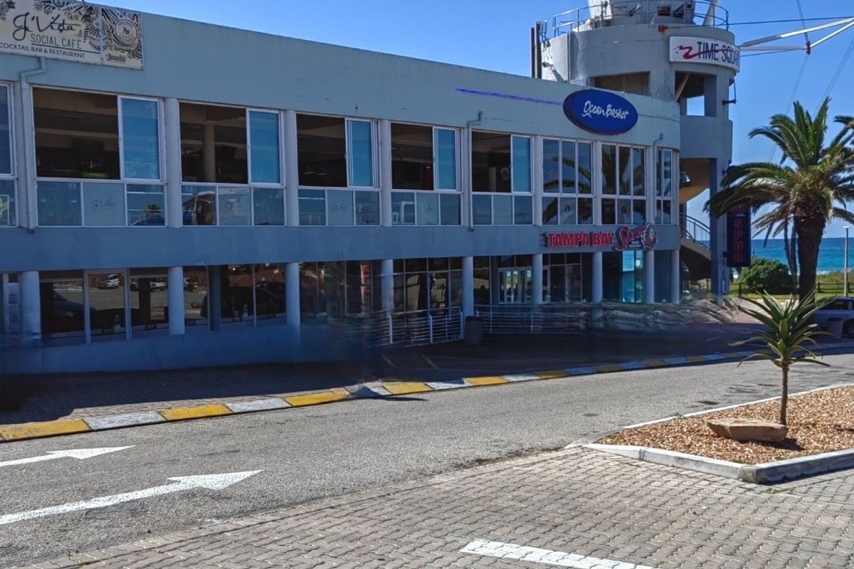 Front exterior view of a commercial building featuring large glass windows, structural columns, and prominent signage, situated near a paved parking area.