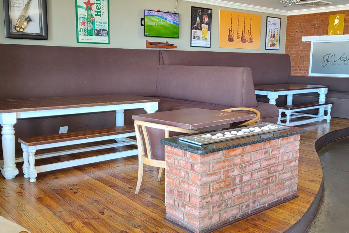 A commercial lounge area featuring raised timber flooring, a central brick fireplace, and integrated booth seating against a feature brick wall.