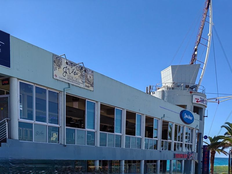 Exterior view of a commercial building featuring large glass windows, prominent signage for a social cafe and restaurant, and an adjacent structural tower.