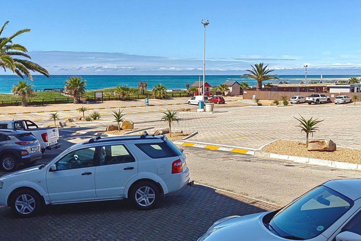 A view of a paved commercial parking area with landscaped garden beds, overlooking the nearby coastline and ocean.