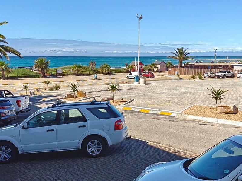 A view of a paved commercial parking area with landscaped garden beds, overlooking the nearby coastline and ocean.