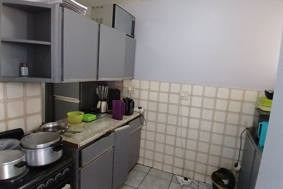 A compact kitchen featuring built-in cabinetry, tiled backsplash, and tiled flooring, offering a functional layout with potential for modernization.