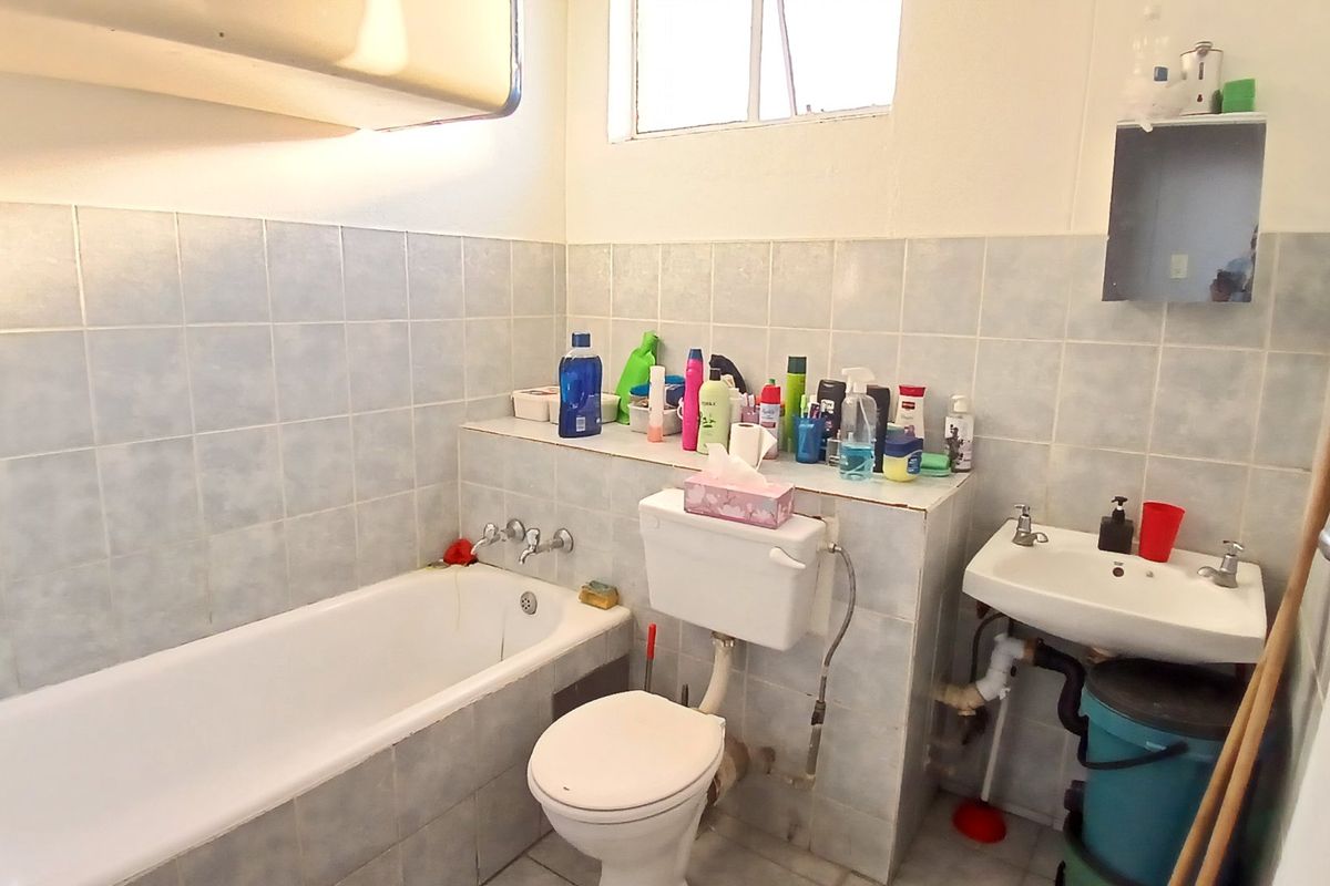 A functional bathroom featuring a bathtub, toilet, and pedestal basin with tiled walls and flooring, offering potential for modernization.