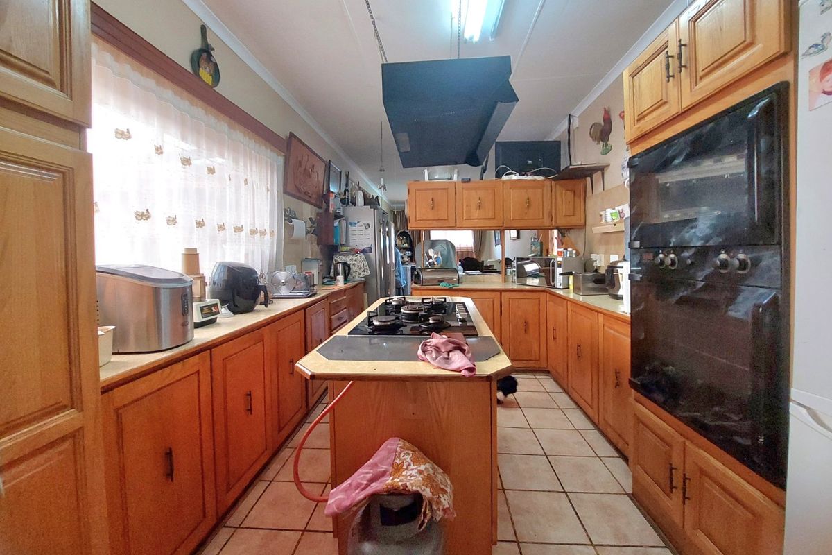 A dated kitchen featuring timber cabinetry, a central island with a gas cooktop, built-in oven, and tiled flooring throughout.