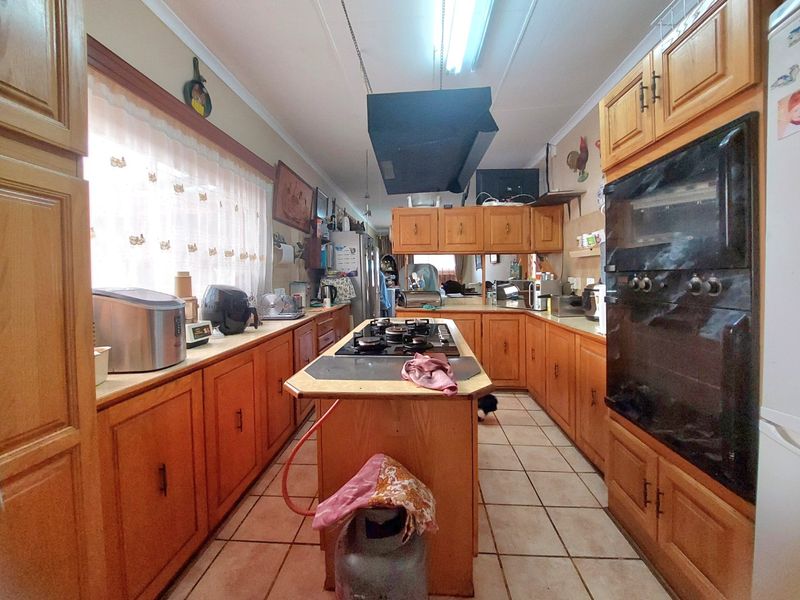 A dated kitchen featuring timber cabinetry, a central island with a gas cooktop, built-in oven, and tiled flooring throughout.