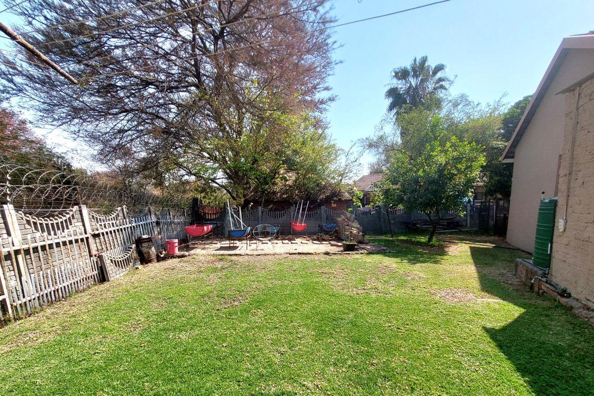 A spacious rear garden featuring a lawn, paved patio area, and secure perimeter walling with razor wire and a water tank.