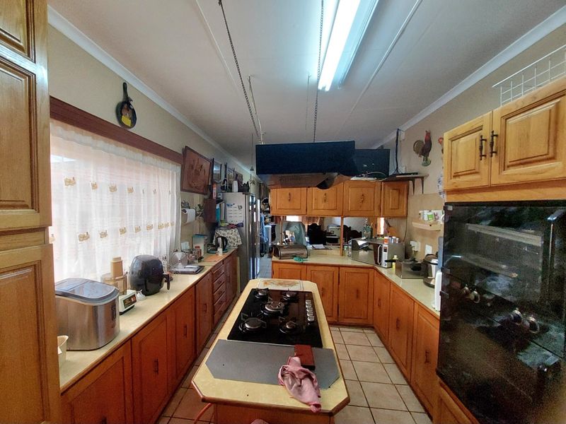 A functional kitchen featuring extensive wooden cabinetry, a central island with a gas hob, built-in oven, and tiled flooring throughout.