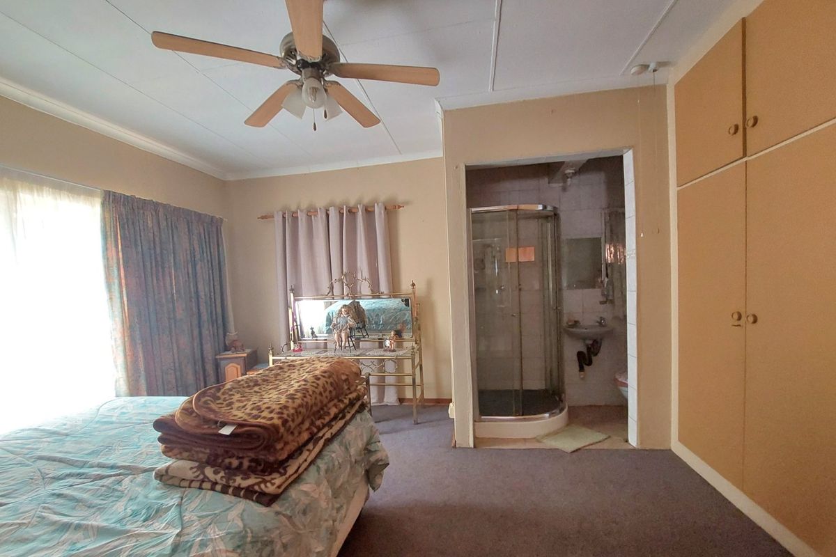 Bedroom featuring built-in cupboards, a ceiling fan, and an en-suite shower room with a glass enclosure and wall-mounted basin.