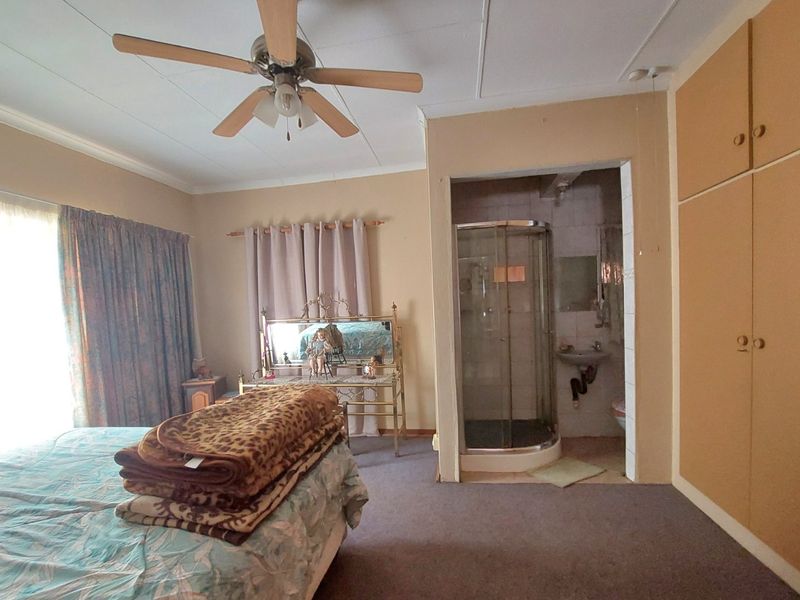 Bedroom featuring built-in cupboards, a ceiling fan, and an en-suite shower room with a glass enclosure and wall-mounted basin.