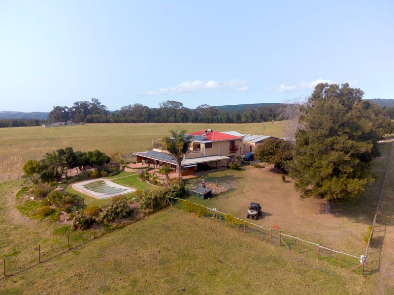 Aerial view of a farm property featuring a main residence with solar panels, a swimming pool, and expansive surrounding grounds.