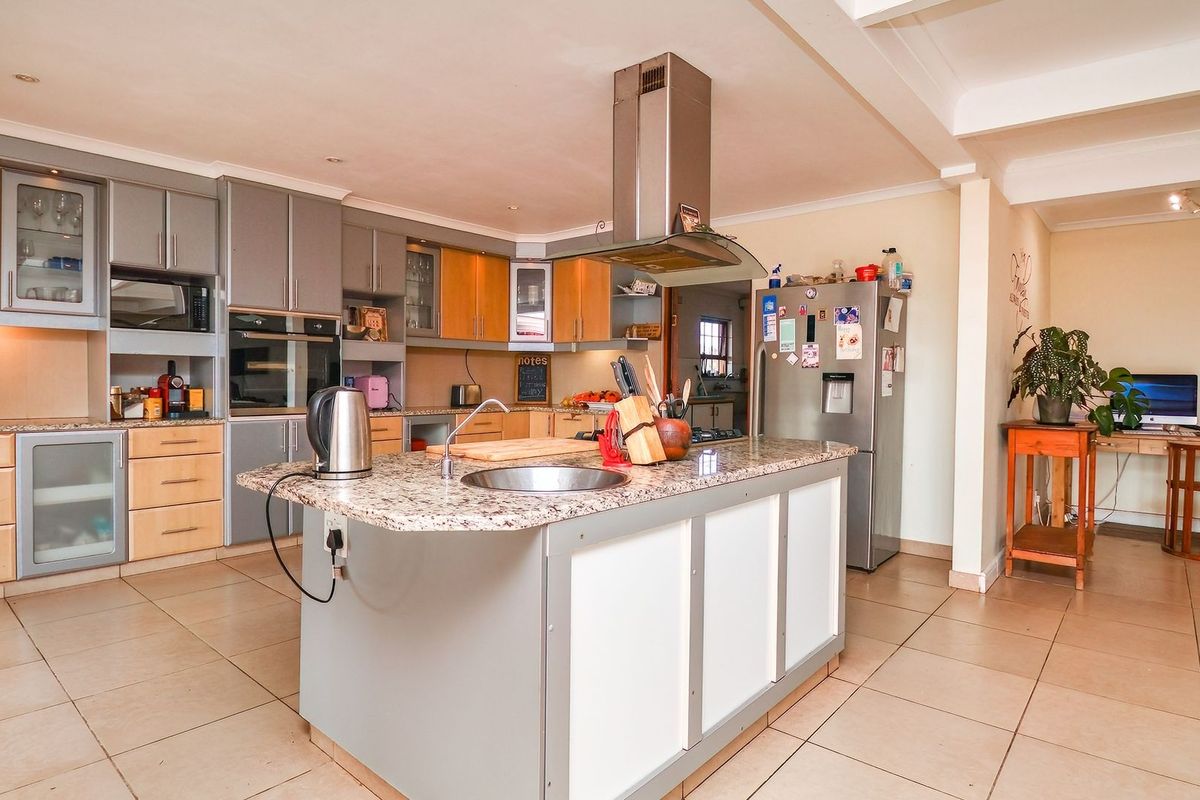 Spacious kitchen featuring a central island with granite countertops, built-in oven, extractor fan, and ample cabinetry, finished with neutral tiled flooring.