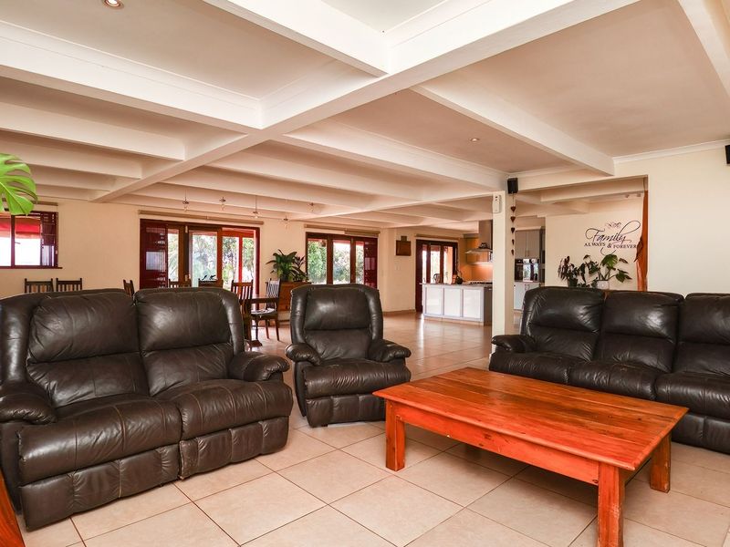 Spacious open-plan living area featuring exposed beam ceilings, tiled flooring, and seamless flow to the kitchen and outdoor patio area.