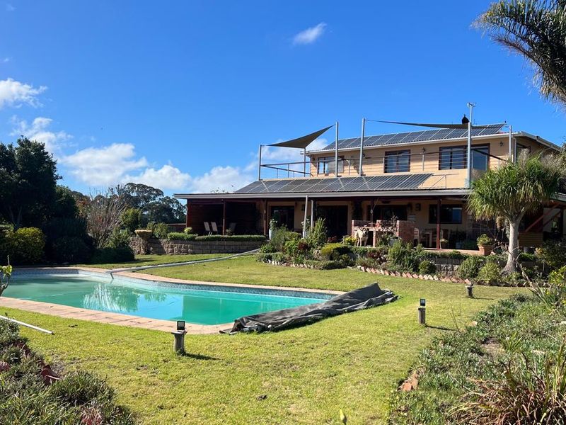 Rear view of the farmhouse featuring a swimming pool, expansive lawn, covered patio, and upper-level balcony with installed solar panels.